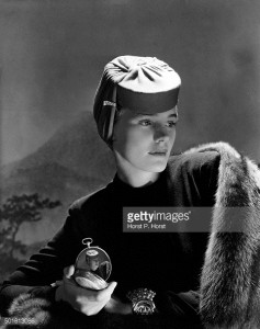 Actress Frances Farmer wearing red jersey hat with jeweled clip, designed by Agn�s, dress, fur stole, and large metal cuff, holding small mirror inset with repeat image of photograph *** Local Caption *** Frances Farmer;
